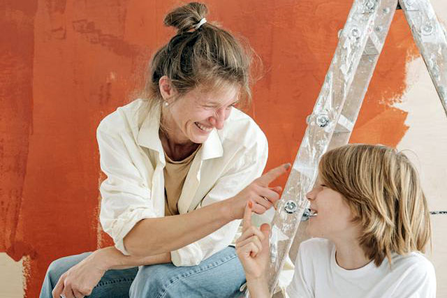 Smiling Mother and son painting their house and showing each other their hands covered in paint
