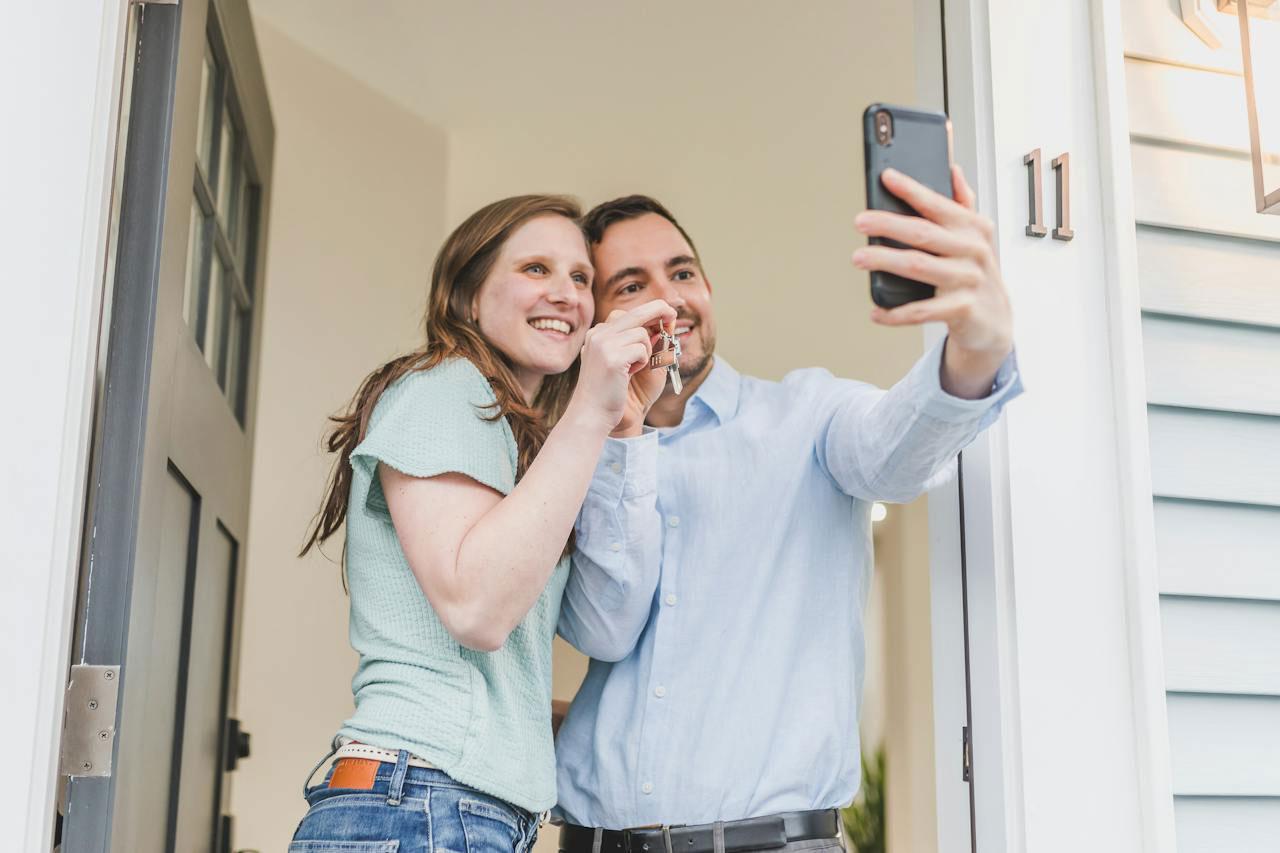 Smiling Young couple taking a selfie in the entryway of their new home and holding house keys in front of them