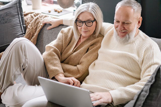 Happy older couple sitting on a couch working on a laptop
