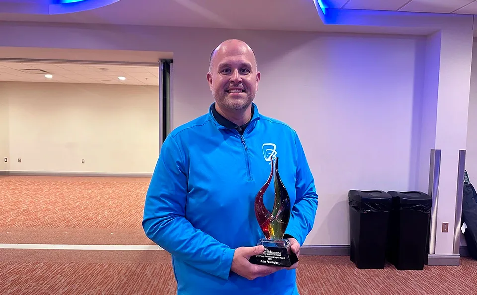Employee Brian Pennington in teal Wildfire logo wear holding Impact Award at banquet hall.