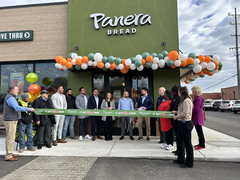 Business members and employees standing outside for Panera's grand opening with ribbon.
