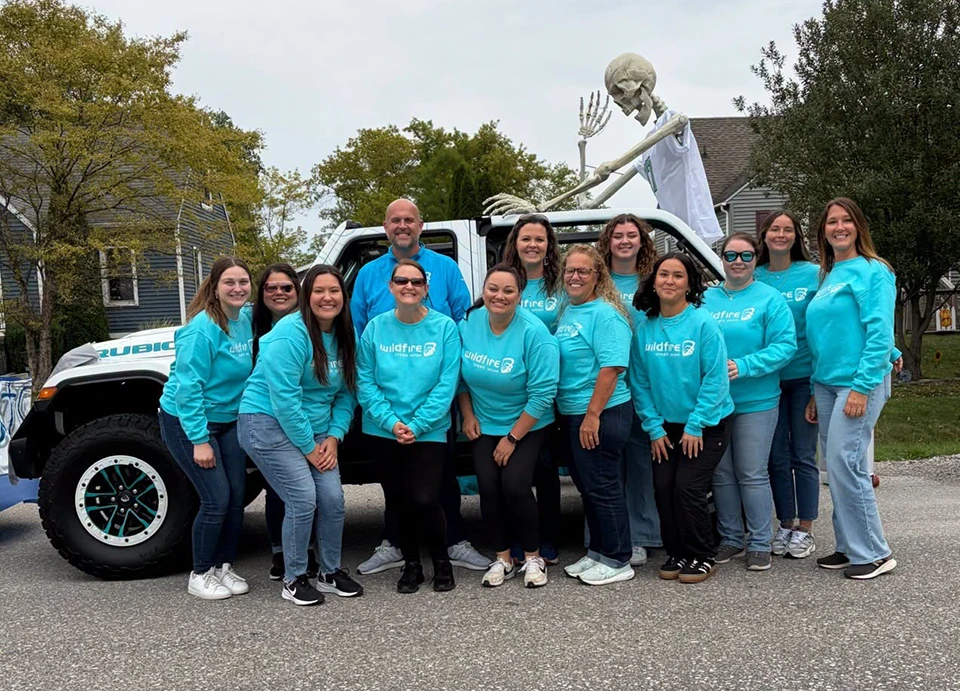 Wildfire employees pose in teal sweatshirts in front of Wildfire Jeep with skeleton in the back.