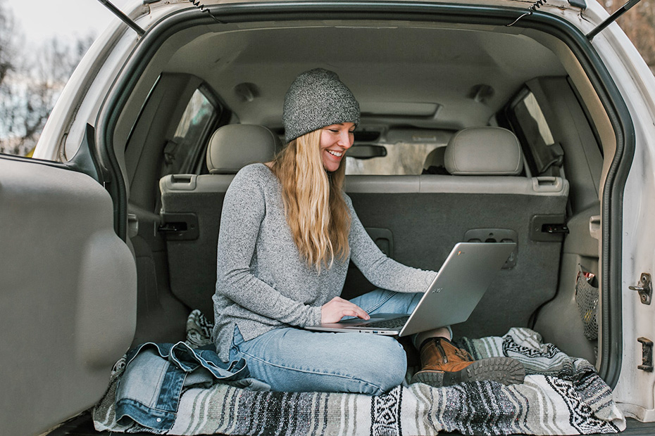 Female in car happily using a laptop