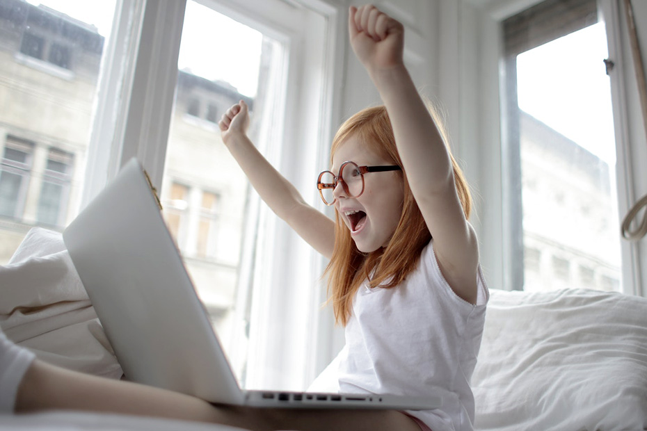 Young girl with red hair on computer cheering