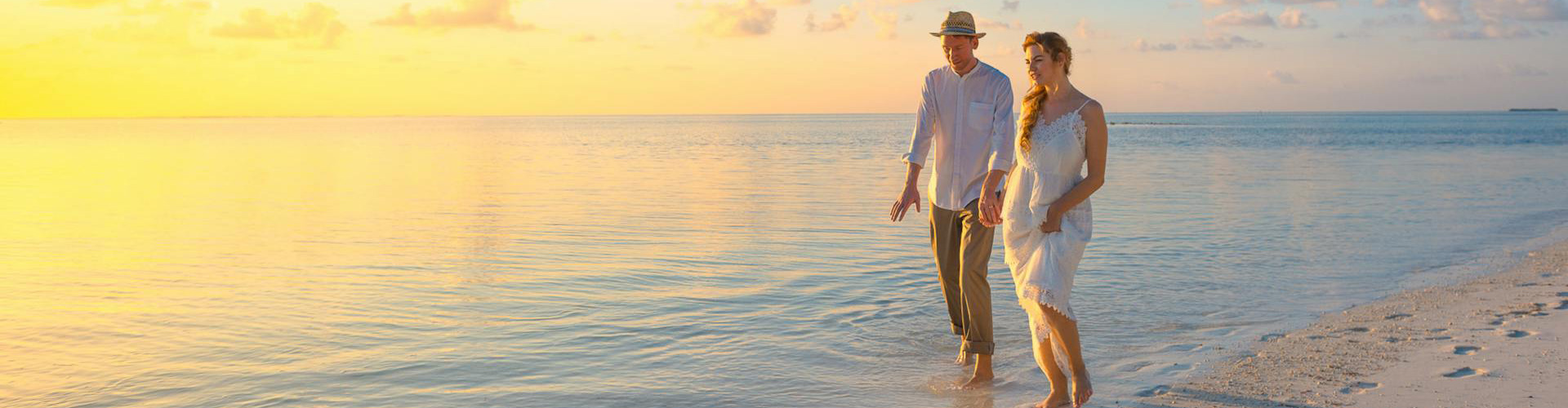Couple walking in white clothing on the beach at sunset Couple walking in white clothing on the beach at sunset