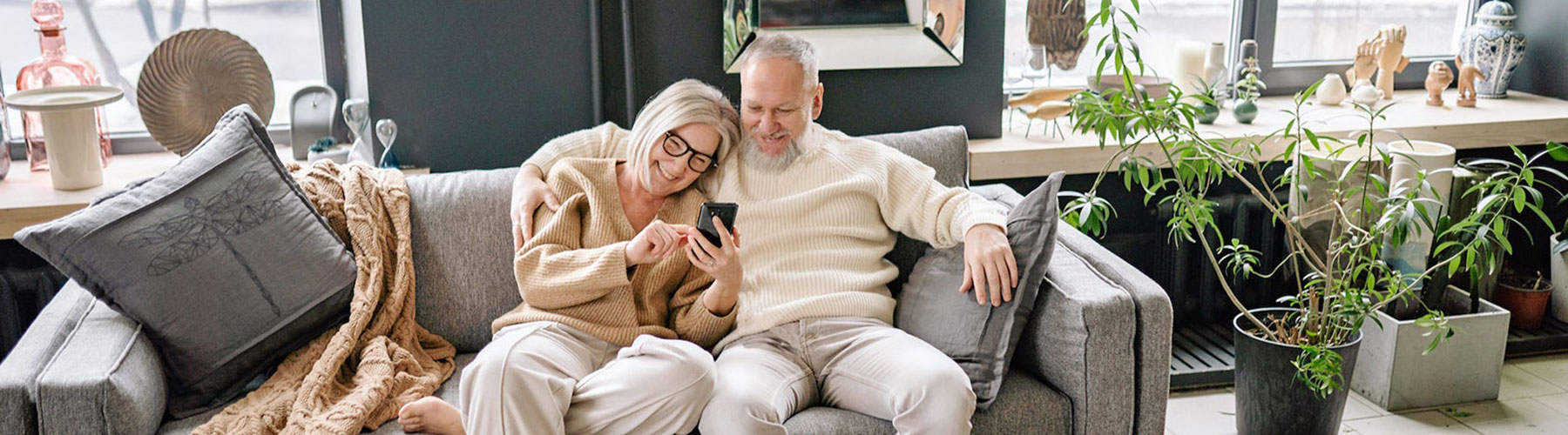 Happy senior couple sitting next to each on couch looking at smartphone
