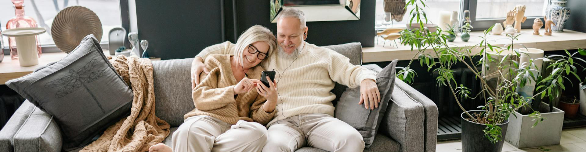 Happy senior couple sitting next to each on couch looking at smartphone Happy senior couple sitting next to each on couch looking at smartphone