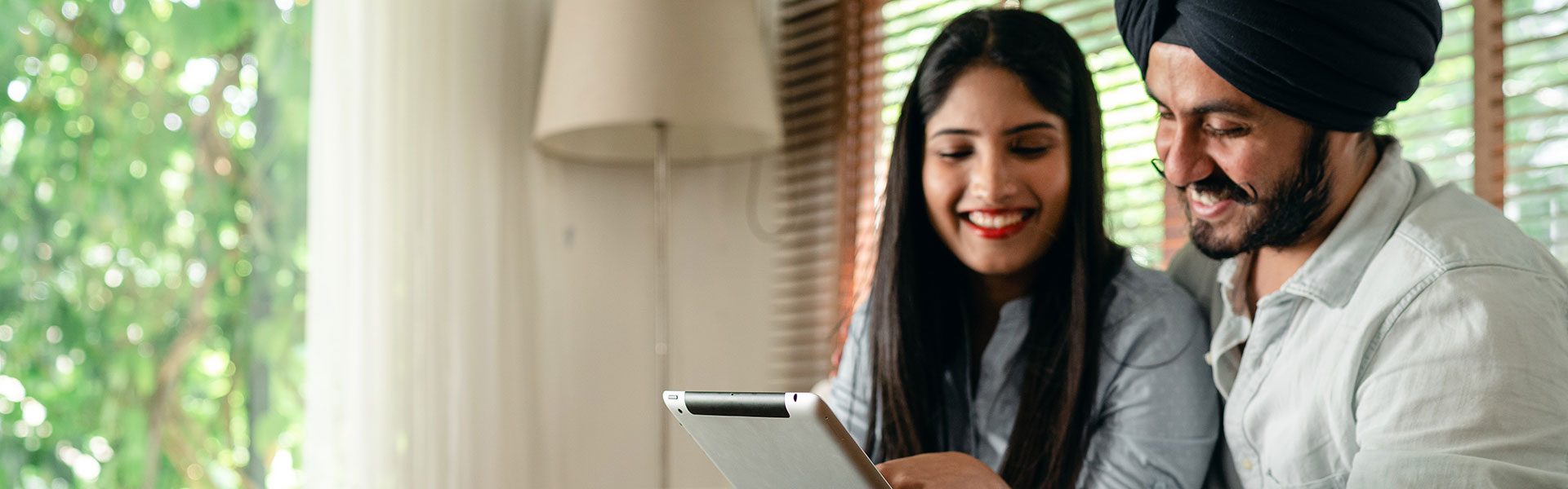 Positive Indian couple using tablet in living room