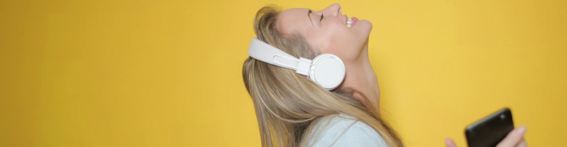 Woman happily listening to music infront of yellow backdrop Woman happily listening to music infront of yellow backdrop