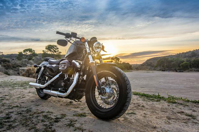 Black Motorcycle sitting on the side of a desert road at sunset