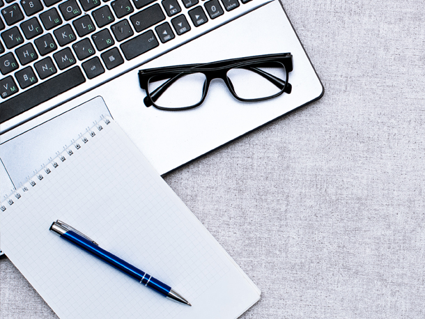 Cardinal Perks Financial Literacy Laptop with glasses, notepad and pen sitting on top