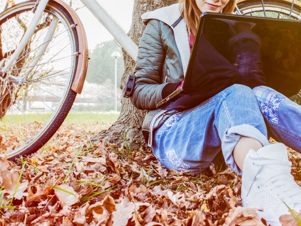 Young woman sitting by a tree on her laptop