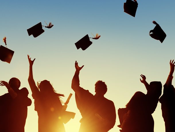 Group of students tossing their caps into the air with the sun in the background