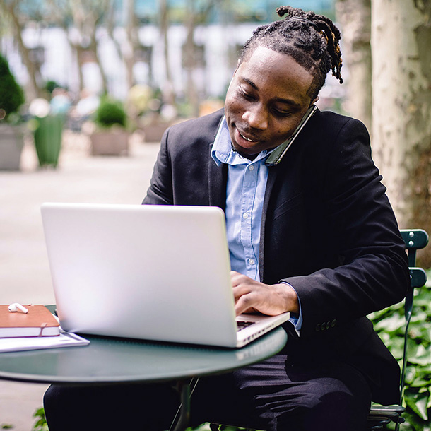 Cheerful black businessman working on computer in park
