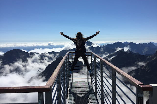 Female standing with her arms out on a mountain overlook above the clouds