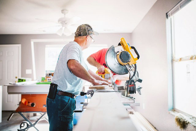 Older man and his son working at a miter saw inside a home