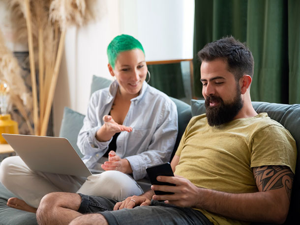 Man using a phone Sitting Beside woman using a laptop on a couch at home