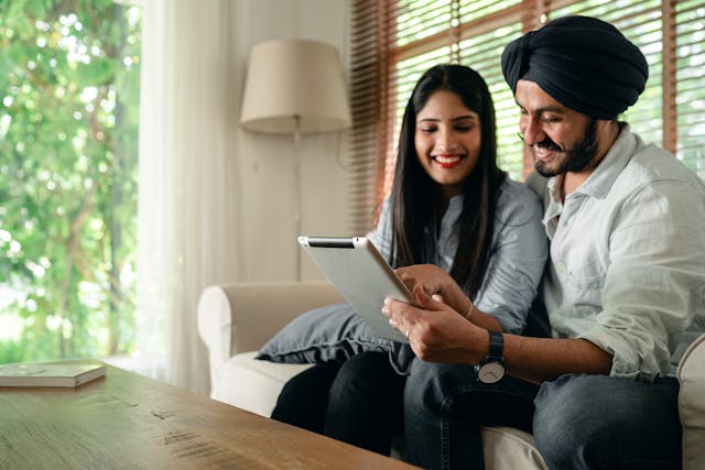 Happy couple sitting on a couch in a well lit living room using an iPad together Happy couple sitting on a couch in a well lit living room using an iPad together