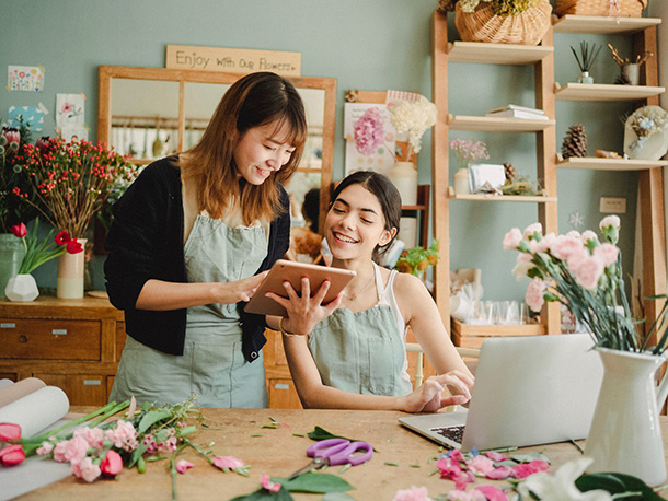 Positive women working with tablet and laptop in floral store