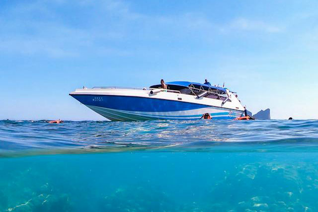 Picture half above water half below water of a speedboat in a lake with people swimming around it Picture half above water half below water of a speedboat in a lake with people swimming around it