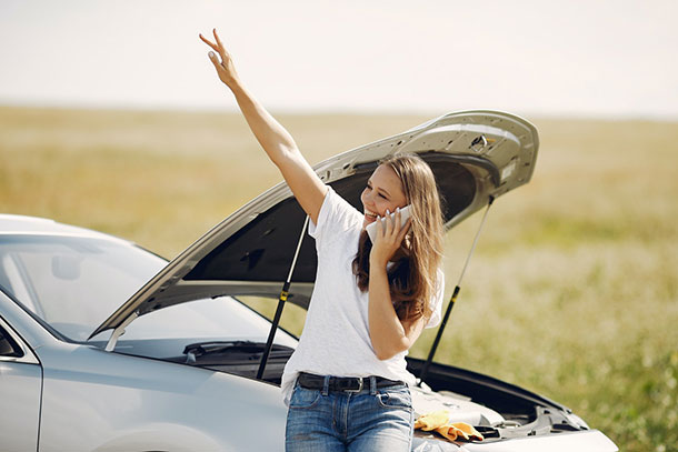 Woman on phone by broken down car waving at someone