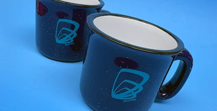 Two navy blue speckled coffee mugs with teal Wildfire logo.