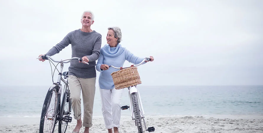 An older couple walking bikes on the beachfront.