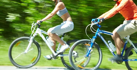 Man and woman riding bikes on rail trail in summer.