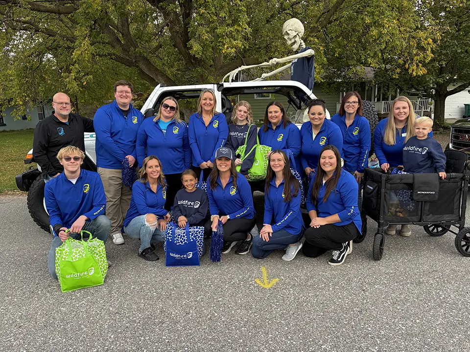 Wildfire employees in blue long sleeve smile in front of Jeep with skeleton at John Glenn High School parade. .