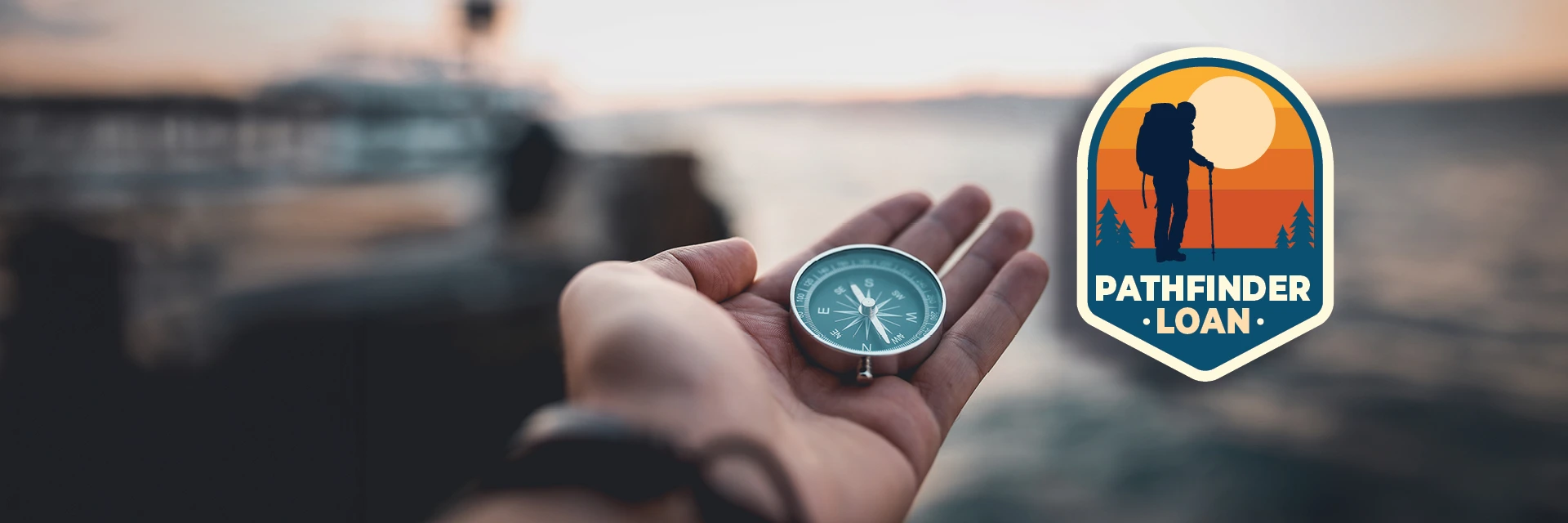 Person holding a compass overlooking the water with a Pathfinder Loan badge next to it.