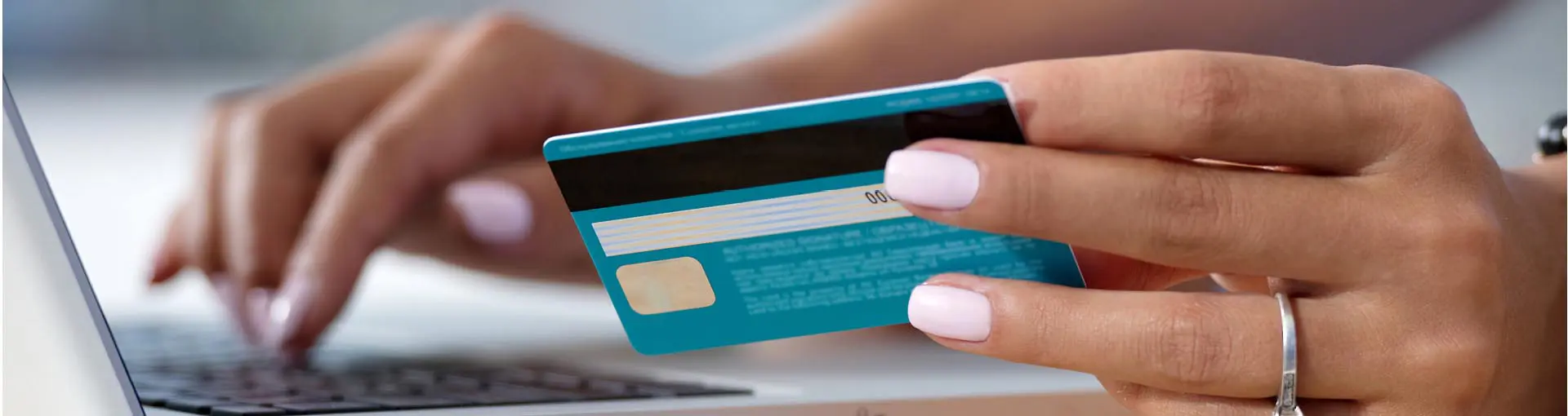 Hands holding a credit card and typing on a laptop.