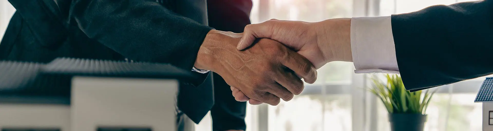 Two business people shaking hands in an office setting, representing a business deal or agreement.