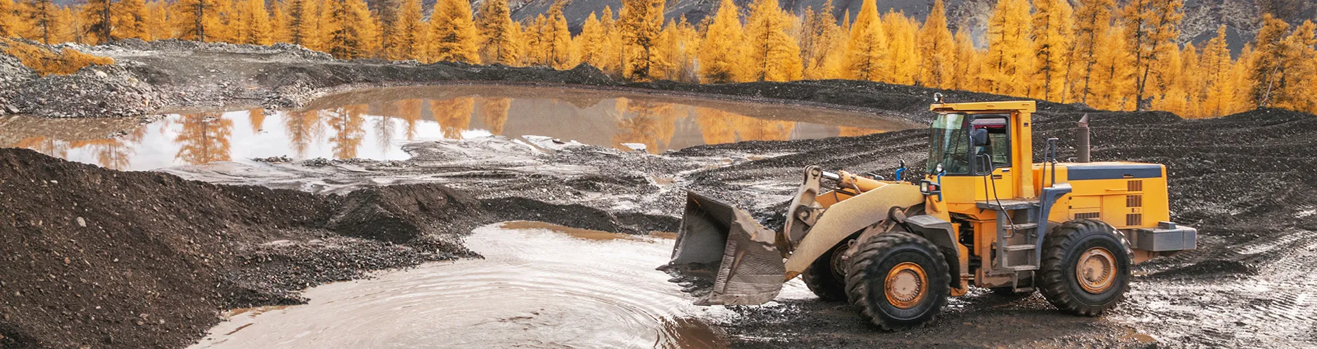 Yellow front loader moving dirt at quarry with yellow fall trees in distance.