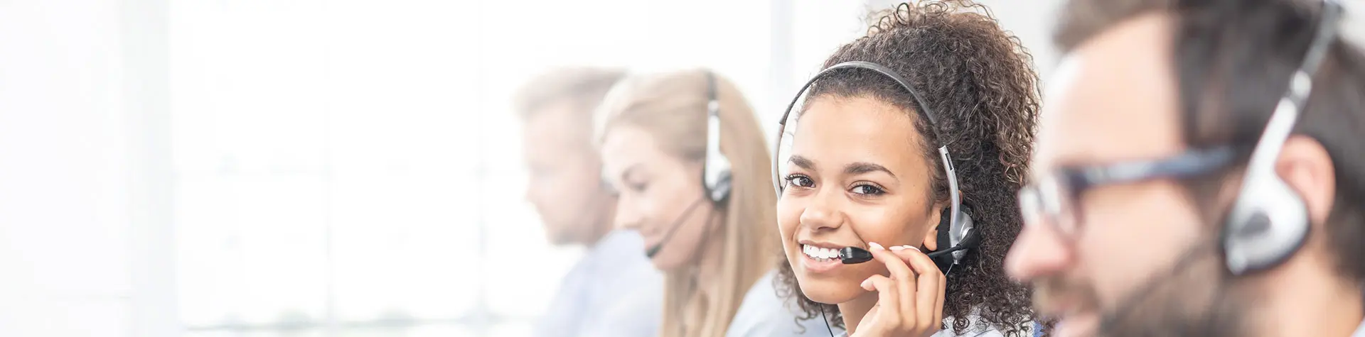Woman between three coworkers on the phone and looking towards camera with smile in contact center.