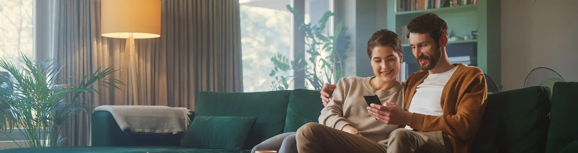 Couple in home sitting on couch looking at smart phone together.