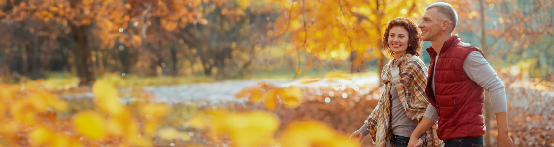 Couple walking through yellow fall leaves in the forest smiling and holding hands.
