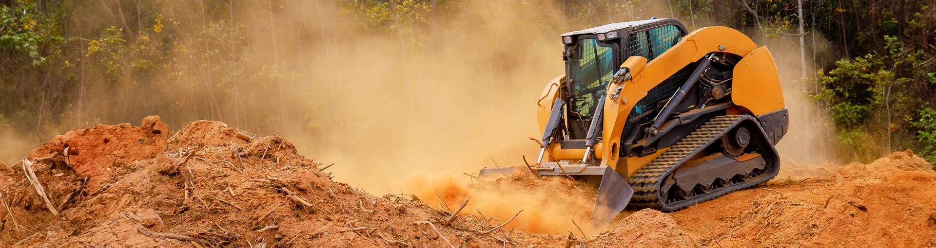Yellow bulldozer equipment moving large piles of red clay sand.