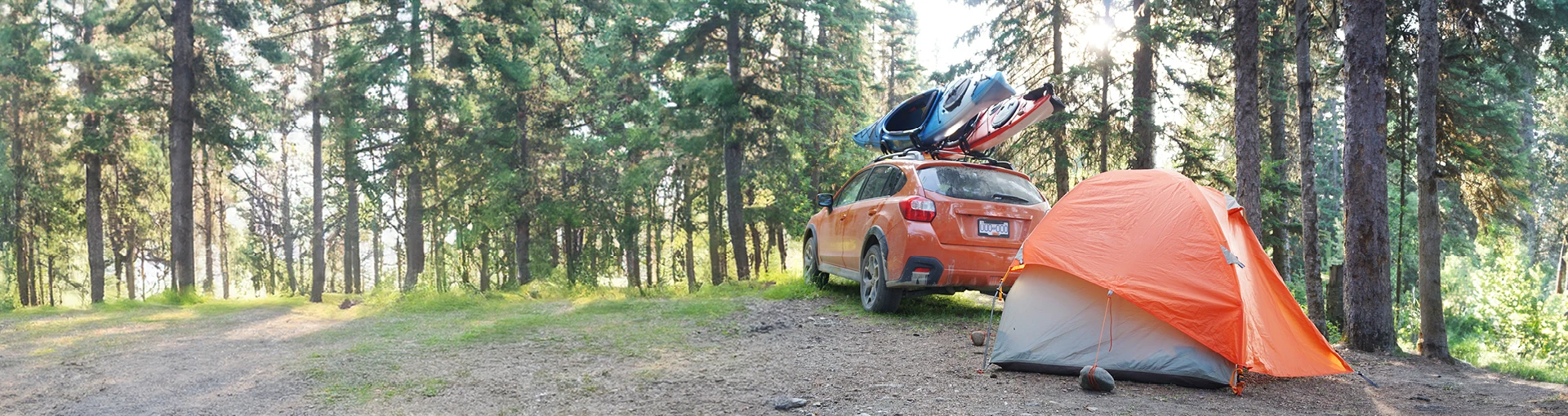 Orange crossover vehicle with kayaks on top next to tent in the Michigan woods.