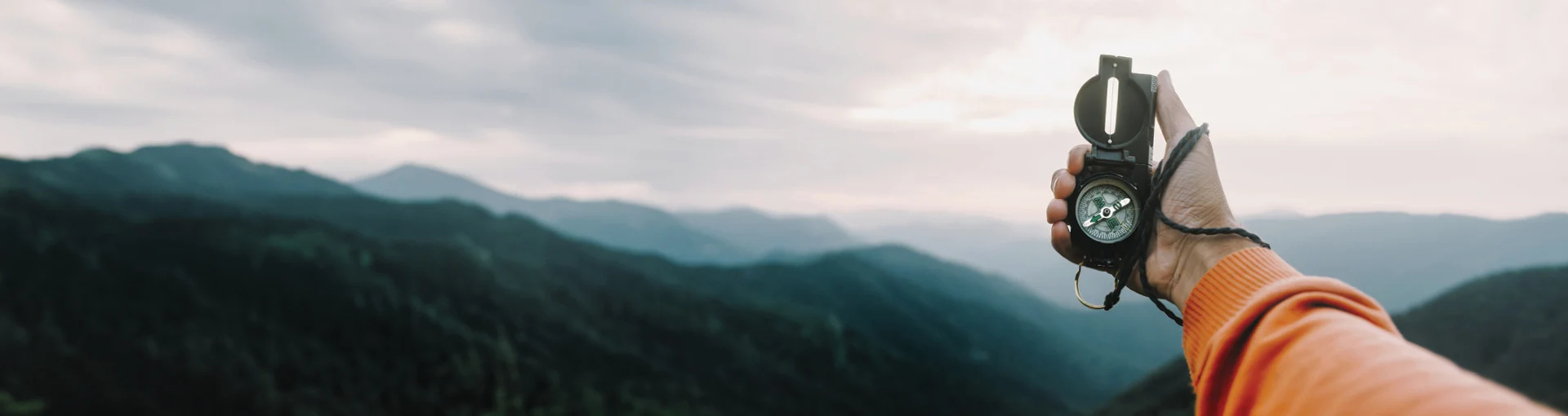 Person Holding a trail compass over the mountains with clouds in background.