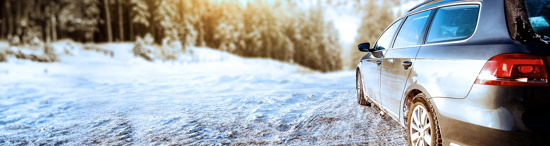 Hatchback car on a snowy two-track with pine trees on both sides.
