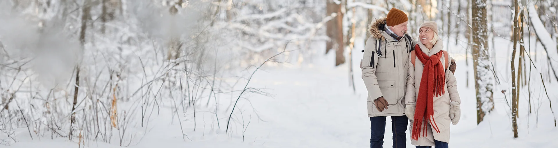 Elder couple with matching coats on a winter hike through the woods.