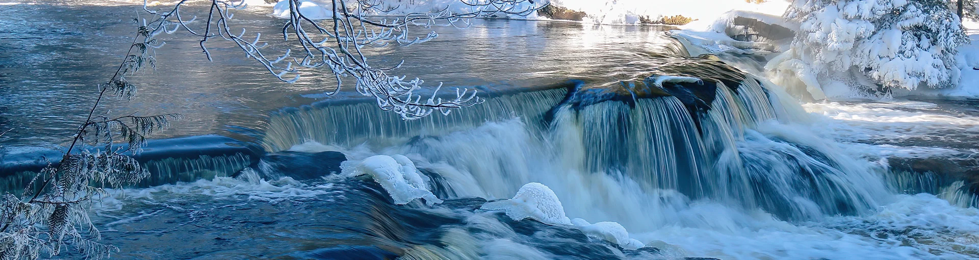 Front of small Michigan waterfall flowing in the winter with snow.