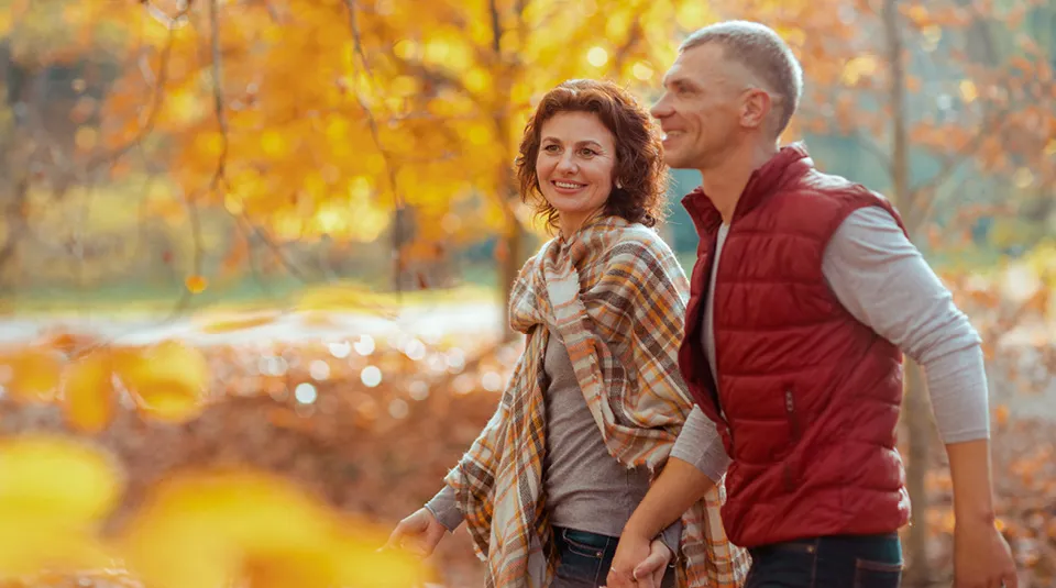 Couple walking through yellow fall leaves in the forest smiling and holding hands.
