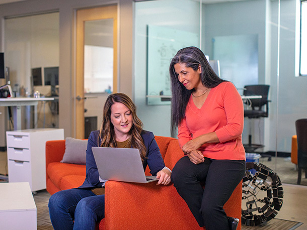 Female co-workers sitting on office couch happily working on computer