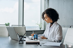 Woman sitting in office with laptop doing paperwork Woman sitting in office with laptop doing paperwork