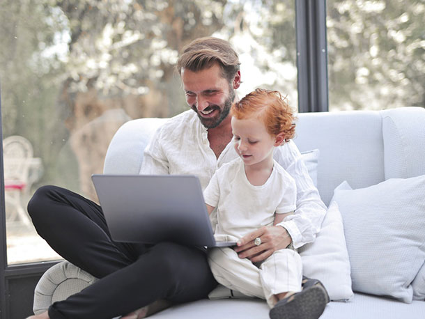 Happy father sitting with child on couch using laptop Happy father sitting with child on couch using laptop