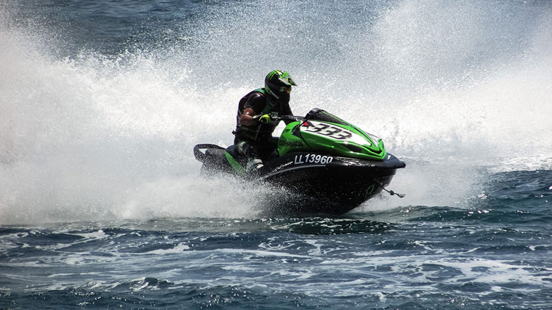 Jet-Ski Man wearing a green helmet driving a green jet-ski through a lake spraying water