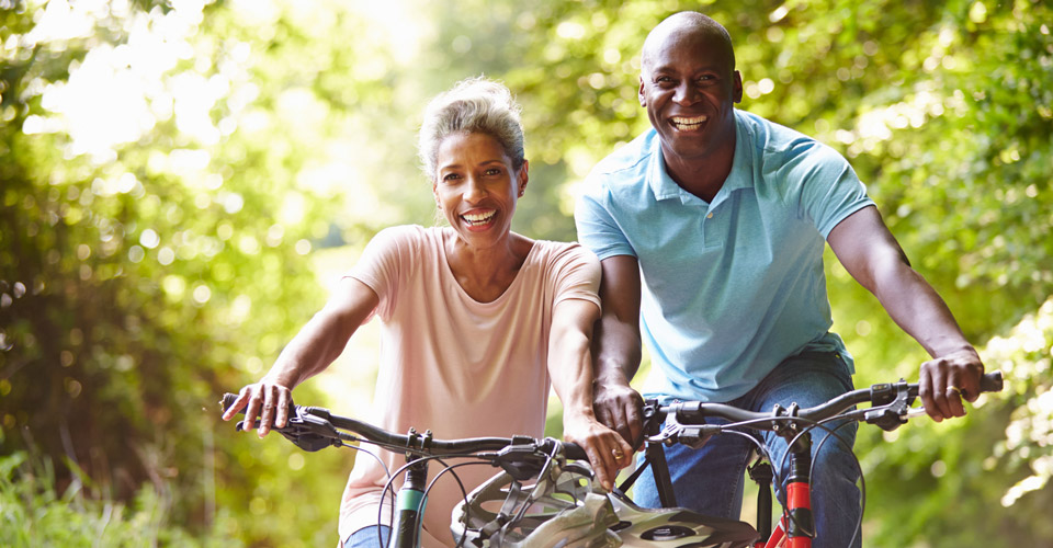 Middle aged couple riding their bikes down a rail trail smiling