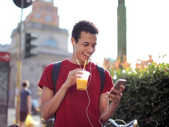 Male outside drinking a smoothie on his phone smiling