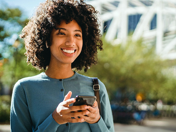 woman with curly hair smiling while holding her phone